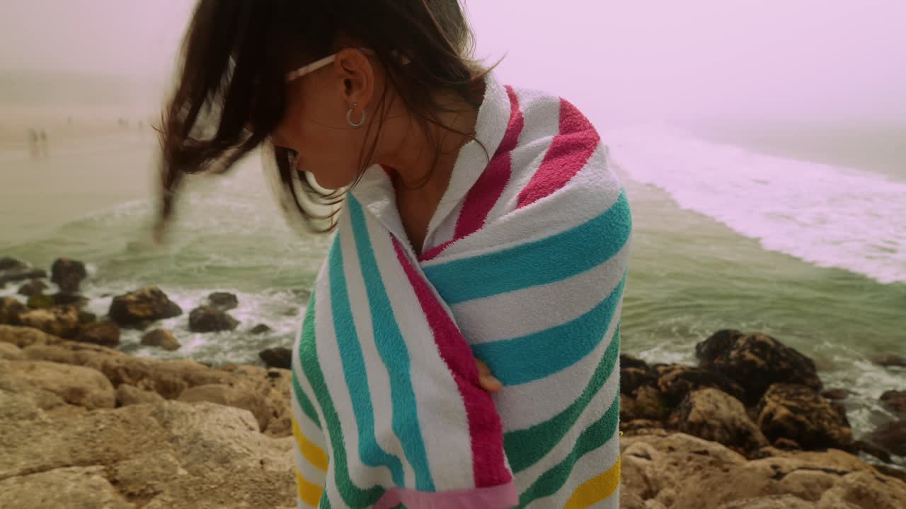 海辺でカラフルなビーチタオルに身を包む若い女性。