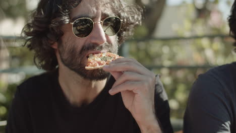 homem de óculos escuros comendo pizza durante festa no terraço com amigos