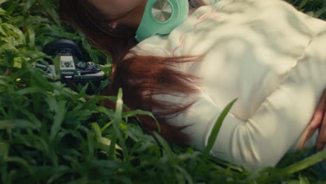 female woman model laying on the grass in the park with old retro vintage camera and headphone relaxing and chilling in her day off