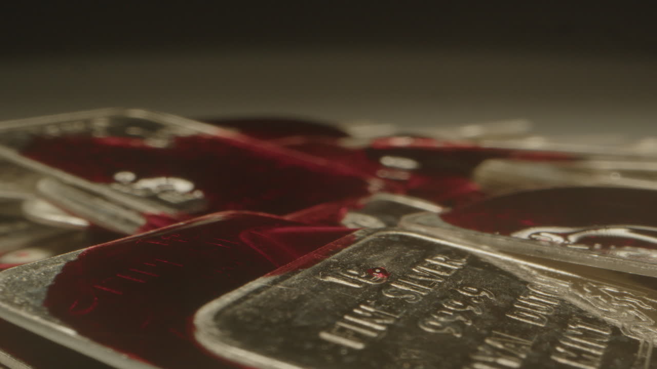 Extreme close up of blood flowing over silver bars. A drop of blood falls on of the plates