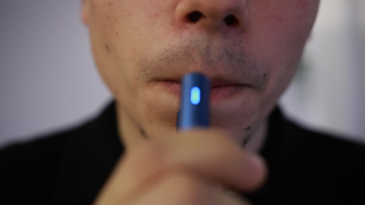 toma de primer plano frontal de un joven vaporizando de un dispositivo de calentamiento de tabaco azul