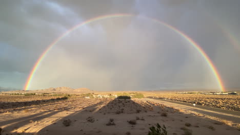 a raven flies towards a bright double rainbow on during a windy, stormy sunset in the desert