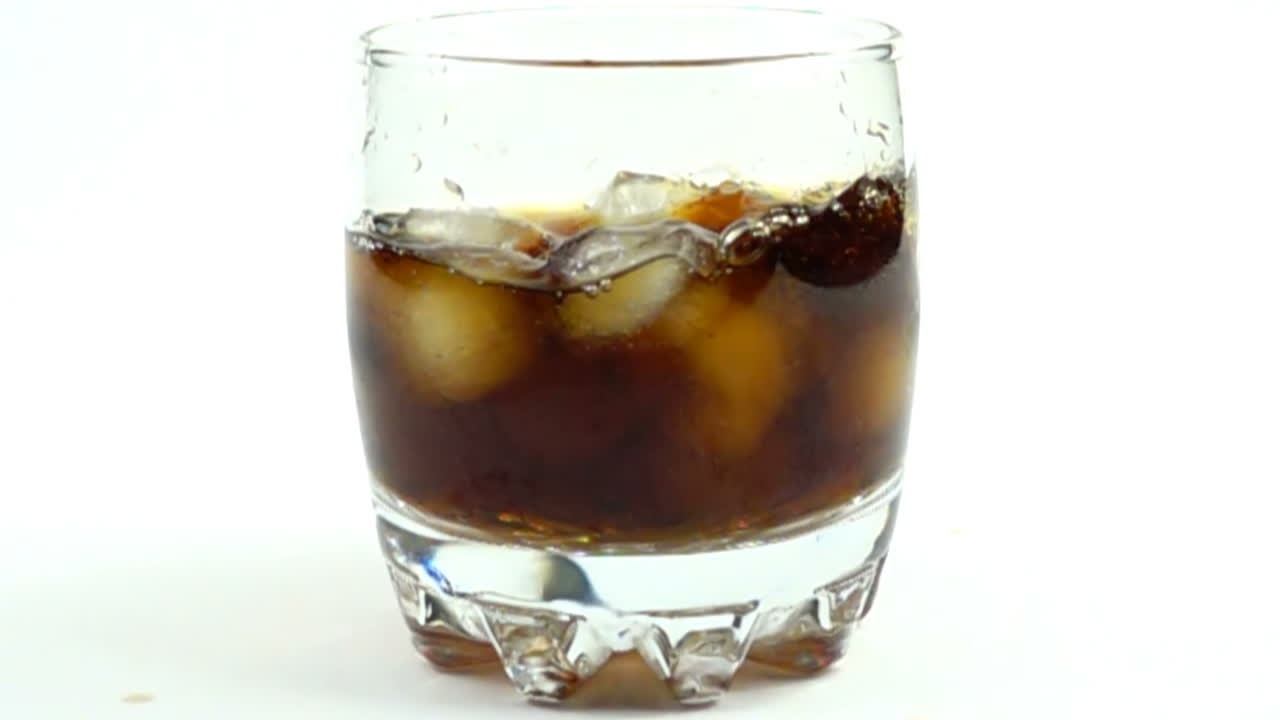 Cubetti di ghiaccio cadono in un bicchiere con una Coca Cola. Rallentatore.