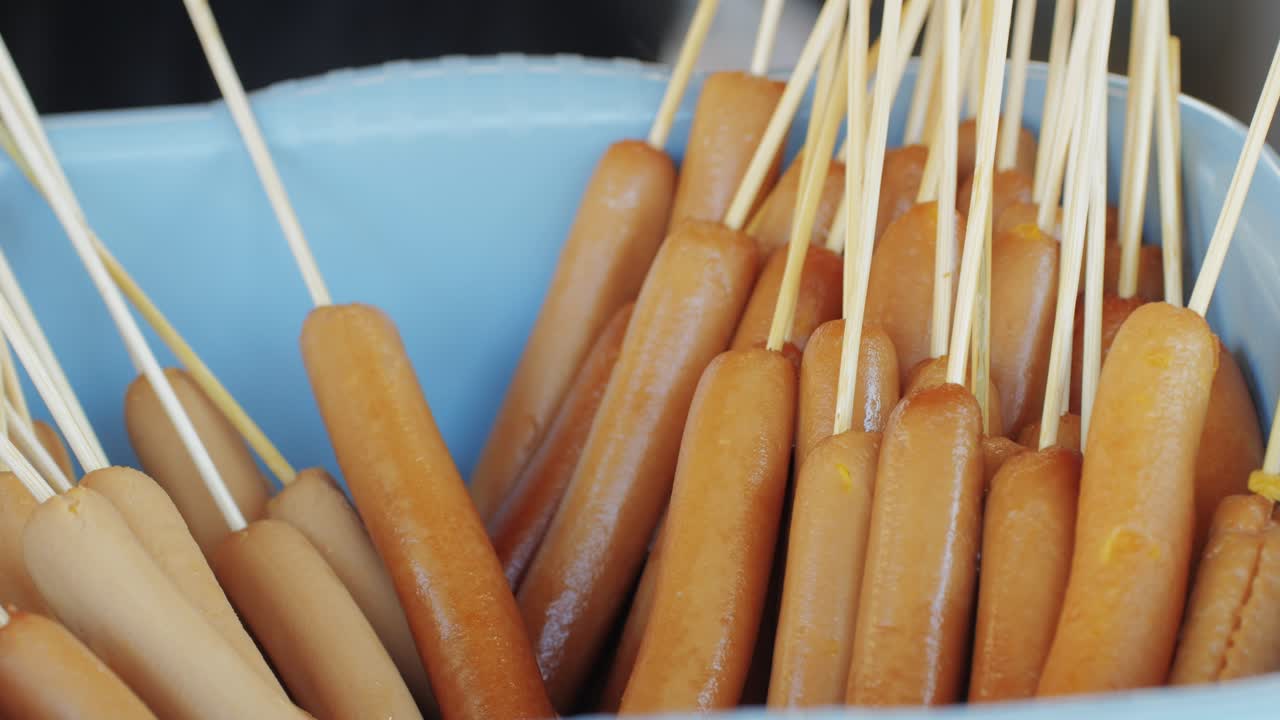 Cooking corn dogs in boiling oil close-up. Traditional asian corndog snacks street food. Fried sausage in breadcrumbs on a stick. Korean Chinese street local market with traditional food. American fast food corndogs with sauce on the top. High quality 4k footage