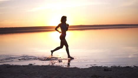 silhouette of a girl running on the water on a sunset or sunrise background. the slender girl runs fast, leaves her stains on the water