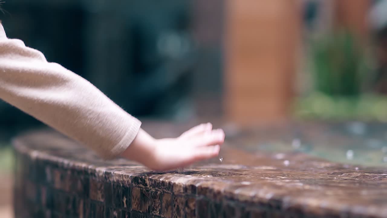 스로우 모션 작은 달 ⁇ 한 소녀는 분수 2 근처에서 물로 놀고 손으로 물을 뿌립니다.