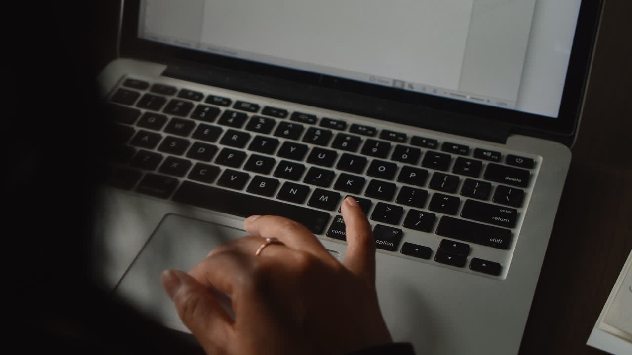 sobre el hombro de una mujer de piel morena escribiendo en el teclado de su computadora portátil mientras la cámara gira a su alrededor en el estudio de su apartamento