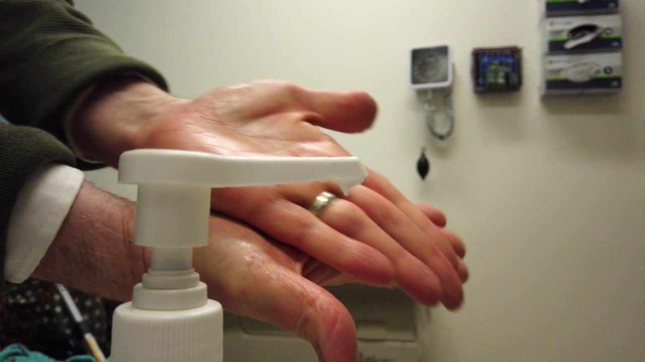 un médico empuja hacia abajo una botella de desinfectante para manos y aplica la loción frotando la sustancia por todas las manos