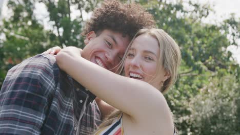 portrait of happy diverse couple embracing in garden on sunny day