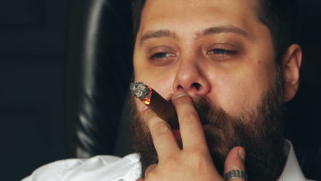 brutal serious man in studio. brutal caucasian serious hipster sitting and smoking cigar