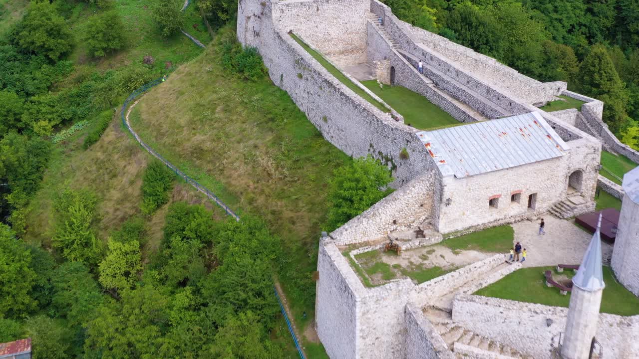 Travnik Castle Fortress in Bosnia and Herzegovina with tourists walking along structure, Aerial pan down reveal shot