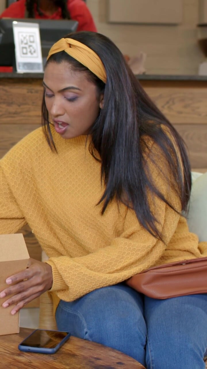 Vertical video: Reaching woman in sweater picking phone at cafe, receiving box and checking order