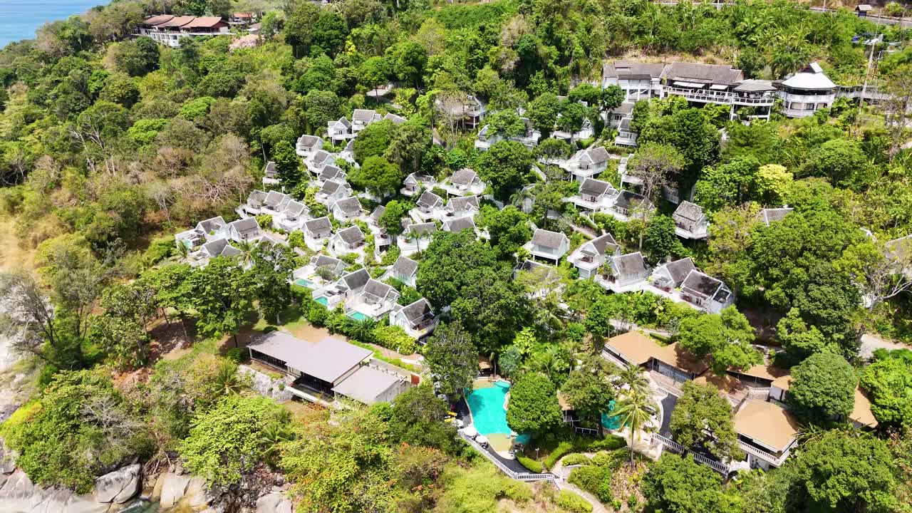 Drone footage captures a lush, tropical resort in Phuket, Thailand, showcasing villas, pools, and vibrant greenery under bright daylight