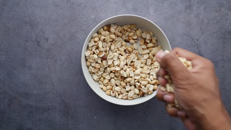 Top-view-of-hand-pick-peanuts-from-a-bowl-on-table