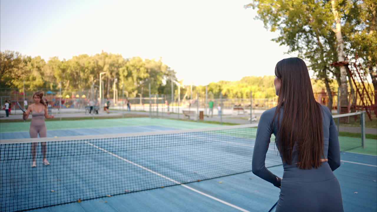 Women playing pickleball with yellow ball and blue paddle at a court