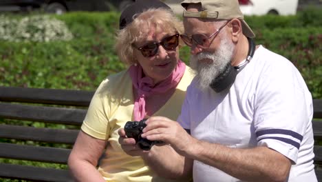 stylish mature couple look the photos at camera sitting on the bench in park