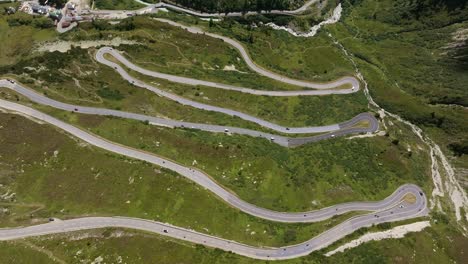 aerial shot of a mountain pass with multiple sharp hairpin turns winding through a green alpine landscape. cars and trucks navigate the serpentine road