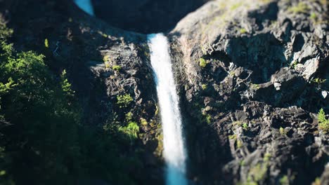 Tilt-shift-view-of-a-serene-waterfall-amidst-the-dense,-green-forest-above-the-Naeroy-fjord