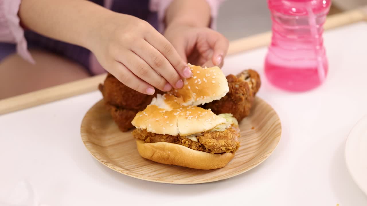 Close-up of child’s hands breaking chicken burger bun on plate, bright indoor lighting
