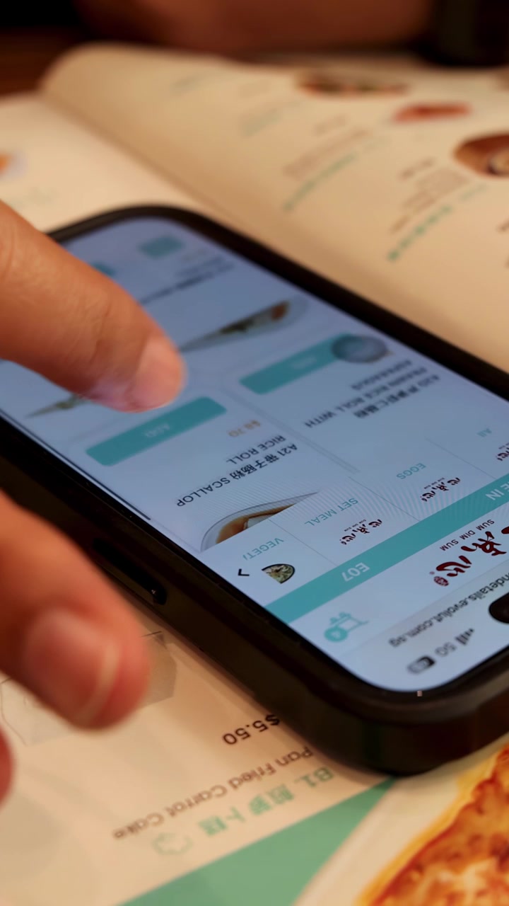 Hand browses food menu on smartphone, warm lighting, shallow depth of field, close-up view