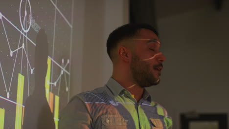 close up of male teacher giving maths or science lesson in school standing at the front of class with projection of graph 1