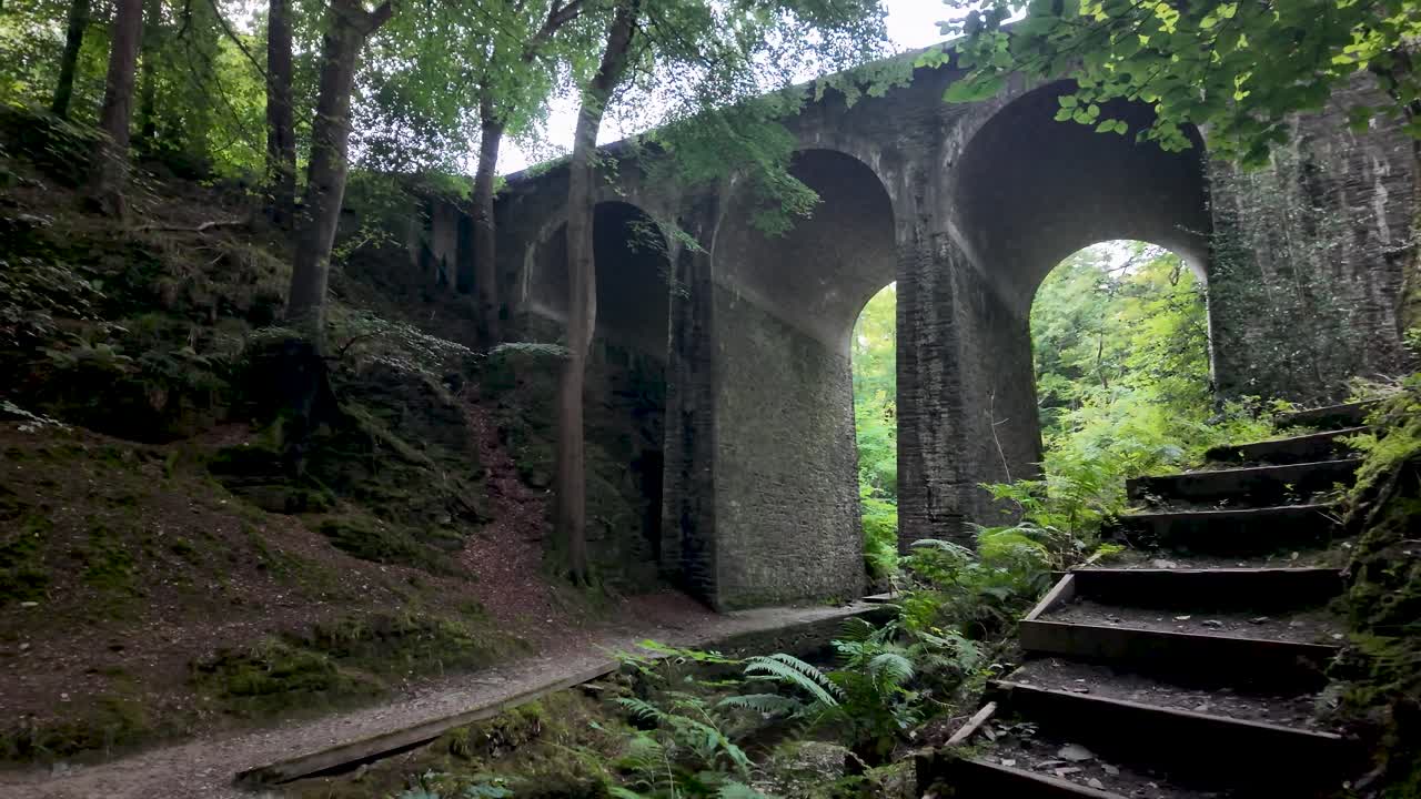 Old stone railway viaduct with wooden stairs in the lush vegetation of Groudle Glen, a picturesque location in Isle of Man
