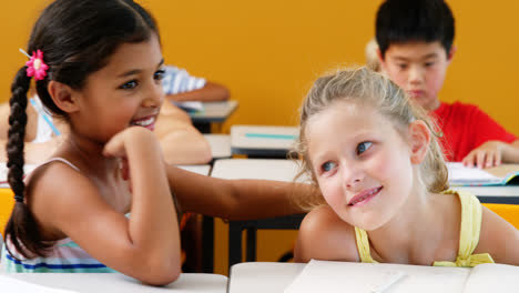 schoolgirl whispering into her friend s ear in classroom