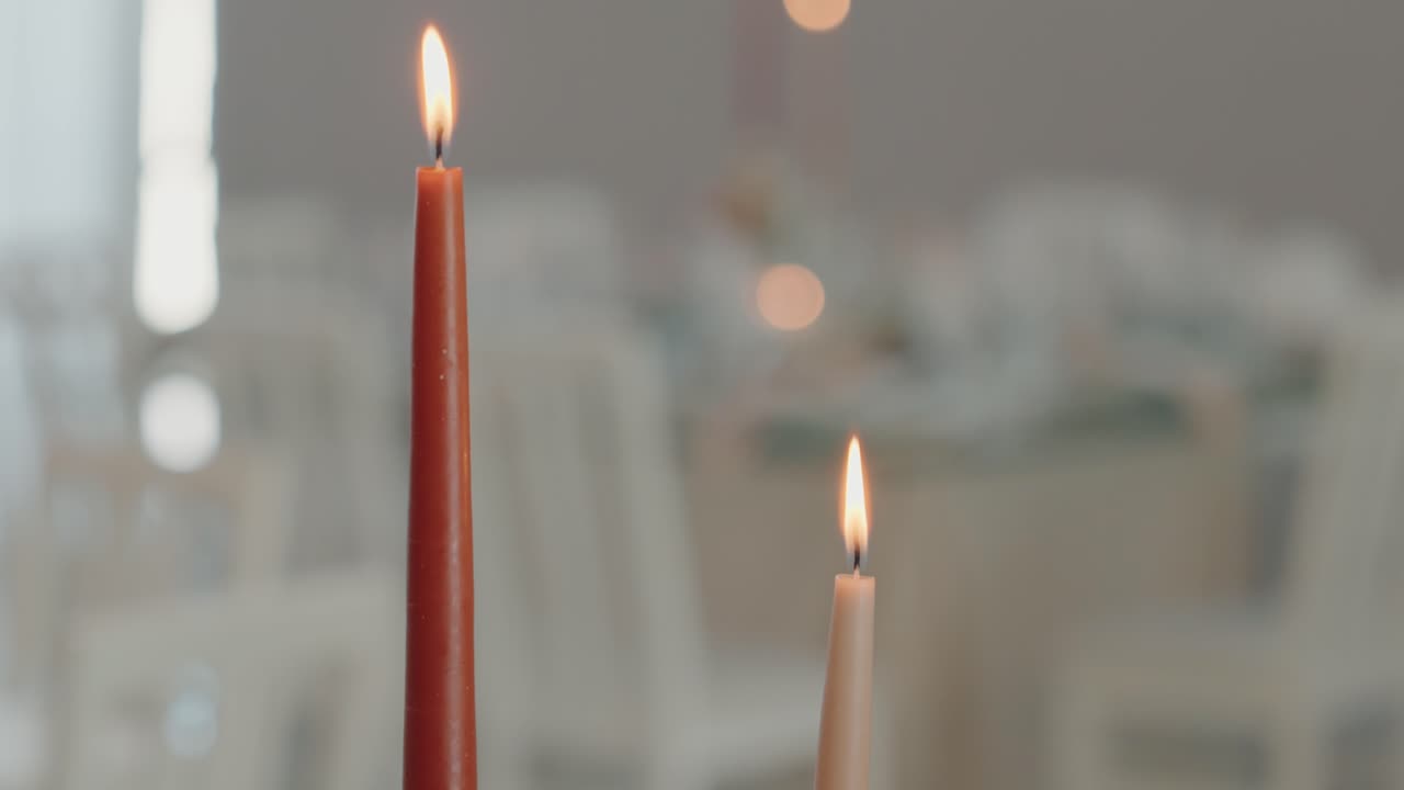 tall candles lit with warm flames at a blurred formal dining setup
