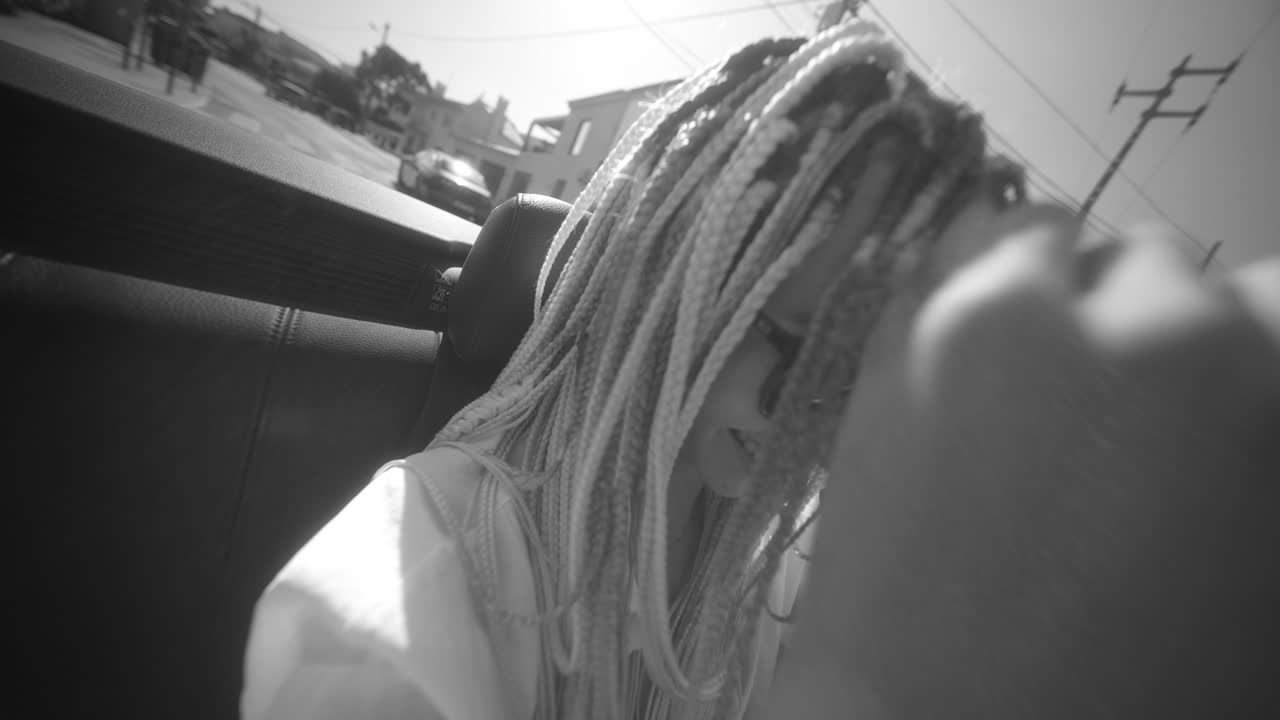 Person with dreadlocks riding in a car, captured in black and white with sun flares