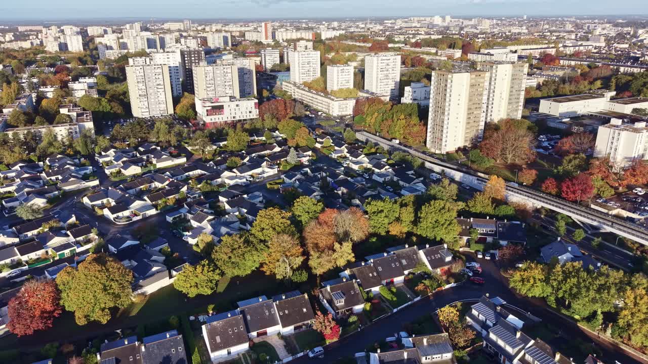 Drone moving forward above Le Blosne district in Rennes, showing residential houses, tall buildings and streets stretching toward the horizon under sunlight