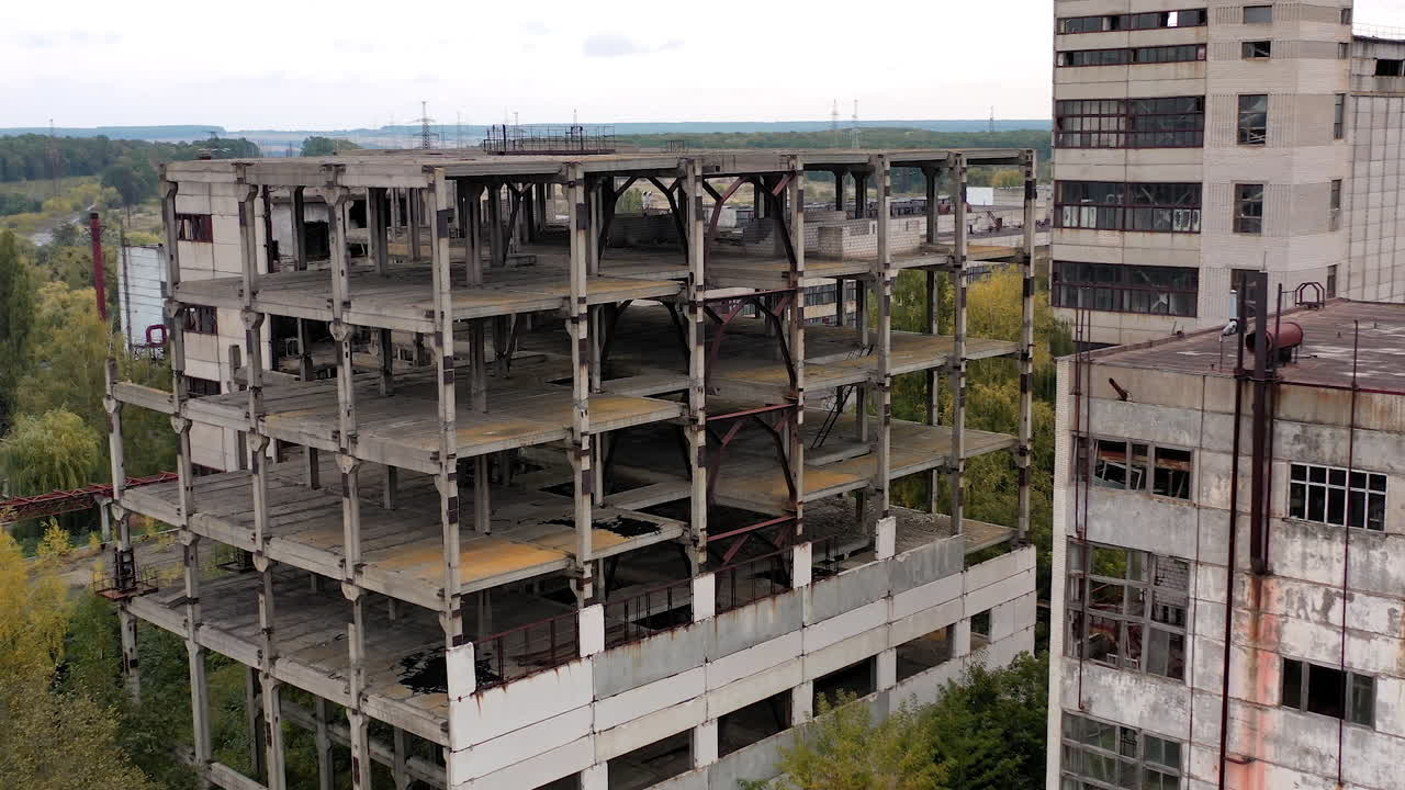 Old factory buildings in rural place. Abandoned territory with ruined warehouses without windows among green nature.
