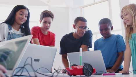 students with male teacher in after school computer coding class learning to program robot vehicle