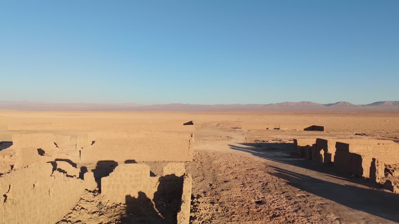 Smooth drone footage flying sideways over the ruins of an abandoned saltpeter refinery in the heart of the Atacama Desert, Chile. Wide view of adobe structures,