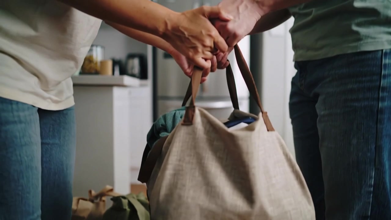 Coppia che si allunga dopo aver fatto i bagagli in maglietta e jeans, afferrando un borsone beige in cucina per trasportarlo
