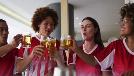 un grupo diverso de amigos felices viendo un juego levantando copas haciendo un brindis en un bar