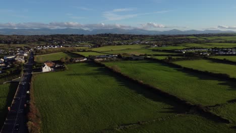 Aerial-view-over-lush-green-sunrise-patchwork-agricultural-Welsh-farming-countryside-town-leading-to-Snowdonia-mountain-range