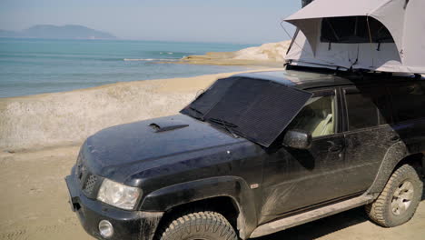 Panel-Solar-Fotovoltaico-Portátil,-Cargando-La-Batería-De-Un-4×4-Junto-Al-Mar-En-Un-Viaje-De-Aventura-Todoterreno-En-Albania