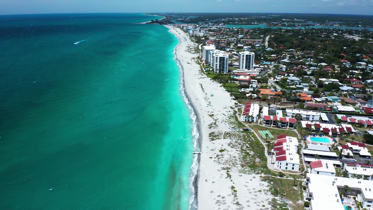 Una città costiera con grattacieli che costeggiano un'ampia spiaggia. Il mare blu vibrante contrasta con la spiaggia di sabbia bianca. Ideale per contenuti urbani e di viaggio.