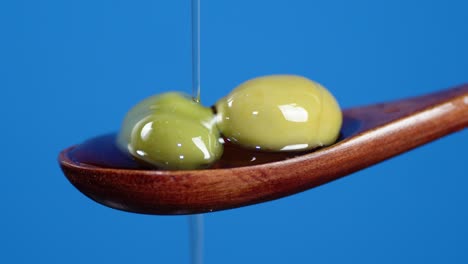 on olives in wooden spoon falling drops of olive oil.