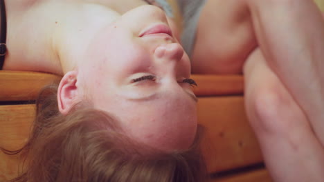 woman resting on wooden bench in sauna with another lady beside her, both relaxing and enjoying soothing moment in peaceful environment