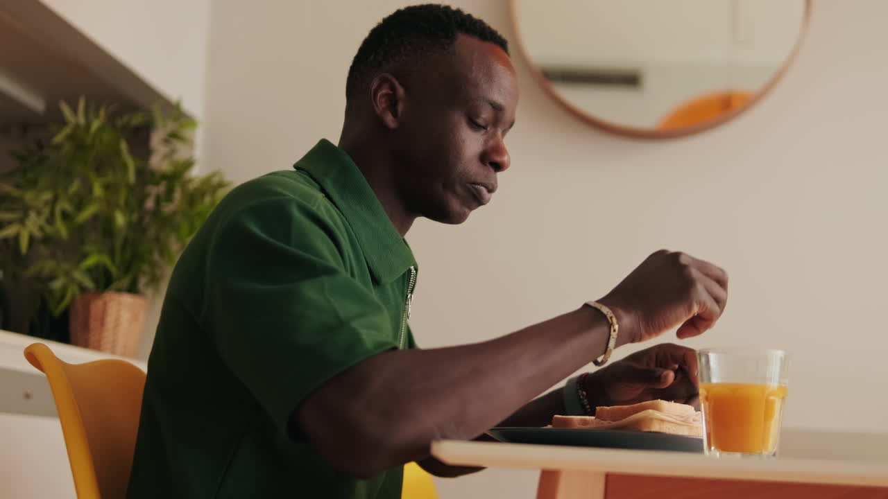 Giovane uomo africano che fa colazione e beve succo d'arancia a casa