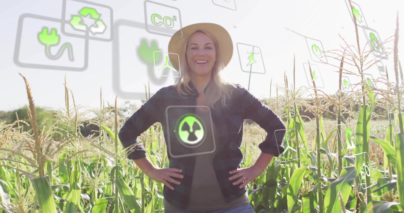 Agricoltrice matura in piedi in un campo di mais che nota icone di energia sostenibile che svaniscono fluttuare intorno a lei.