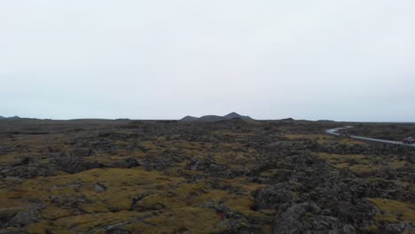 Foggy-rugged-landscape-with-lava-formation-rocks,-car-driving-on-road