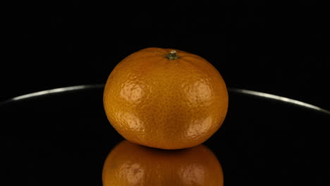 clementine orange fruit reflected in mirror revolves in black room