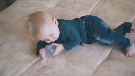 Un-Niño-Lindo-Juega-Con-Una-Botella-Arrastrándose-En-La-Cama-En-Casa