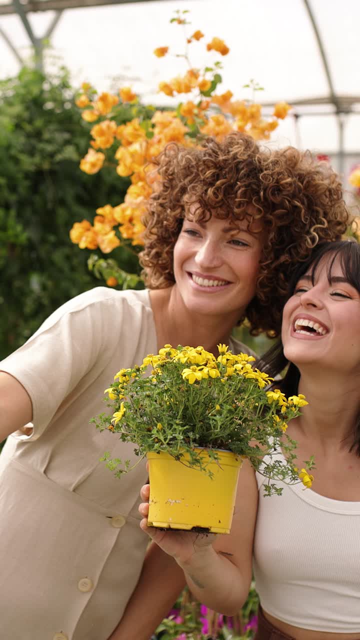 Happy women taking selfies with yellow flowers in greenhouse. Vertical