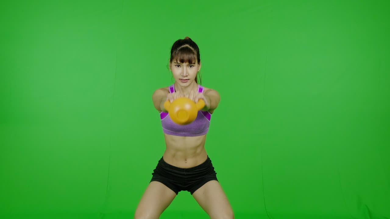 mujer en forma levantando kettlebell en pantalla verde, hacia adelante, ambas manos, vista frontal, clave de croma, tecnología, realidad aumentada. mujer asiática, para superposición gráfica y propósitos de corte.
