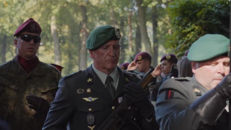 soldiers, led by a man in a green beret, march past saluting troops at a ceremony in oosterbeek war cemetery. oosterbeek, gelderland
