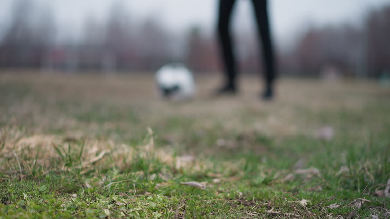 Blurred view of a football being passed between two people on a grassy field, with one person trapping the ball under his foot