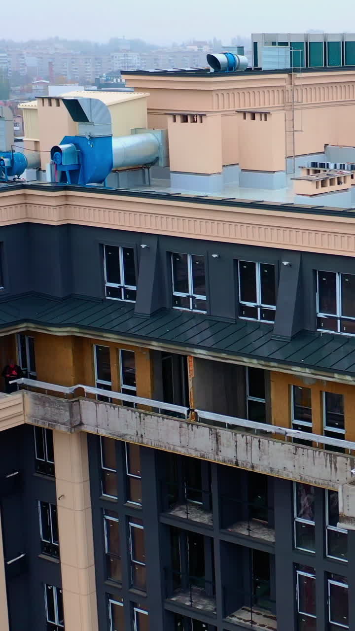 Building of a new tower house. Workers on the roof of multistorey building during the construction on the cityscape. Aerial view. Vertical video